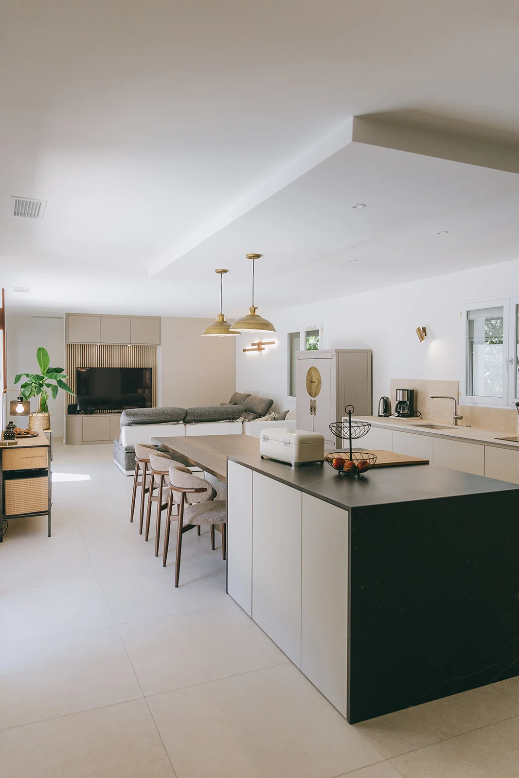 Séjour et cuisine ouverts beige avec îlot noir et suspensions en laiton réalisés à Montpellier