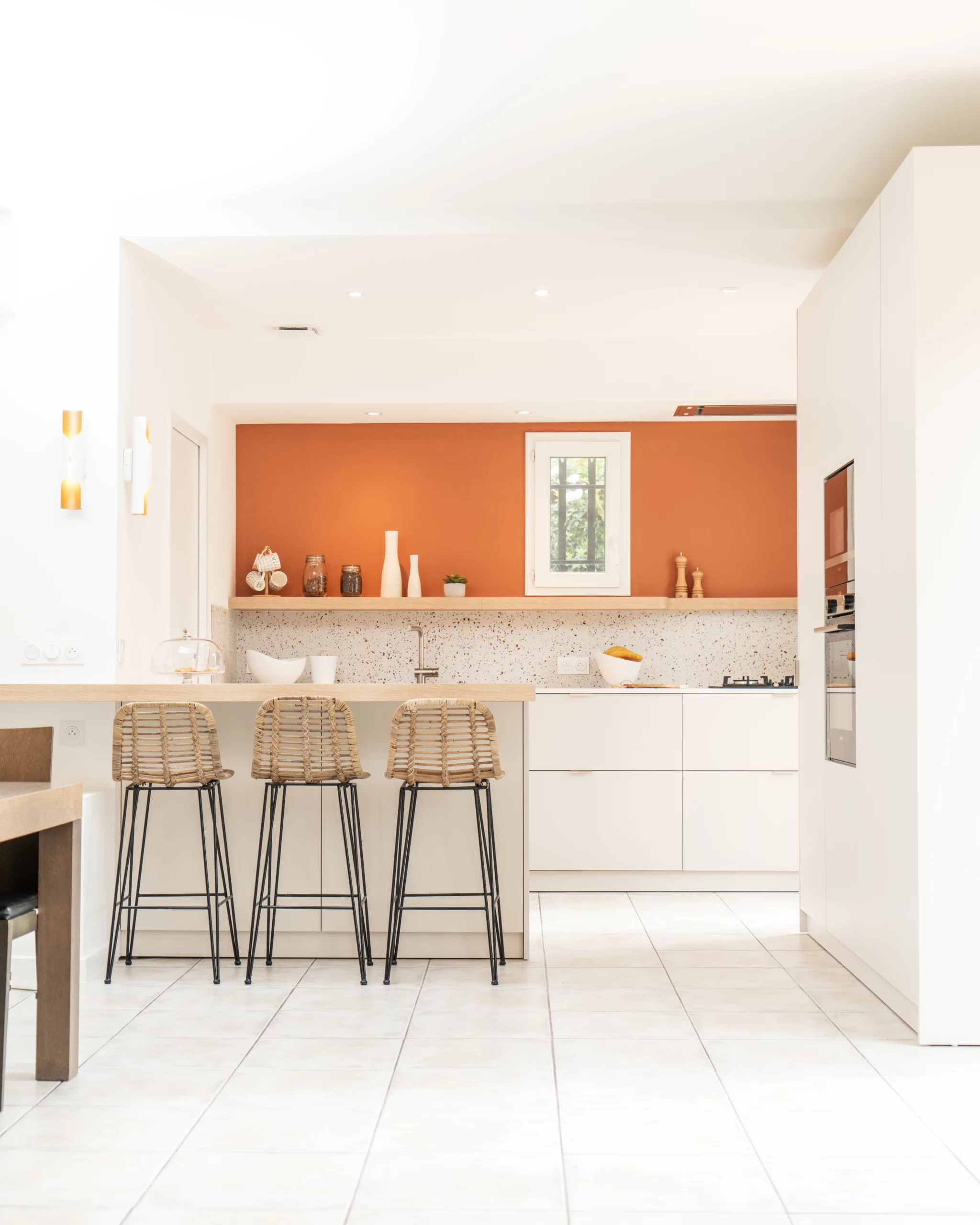 Cuisine ouverte blanche avec mur terracotta et tabourets en rotin à Montpellier